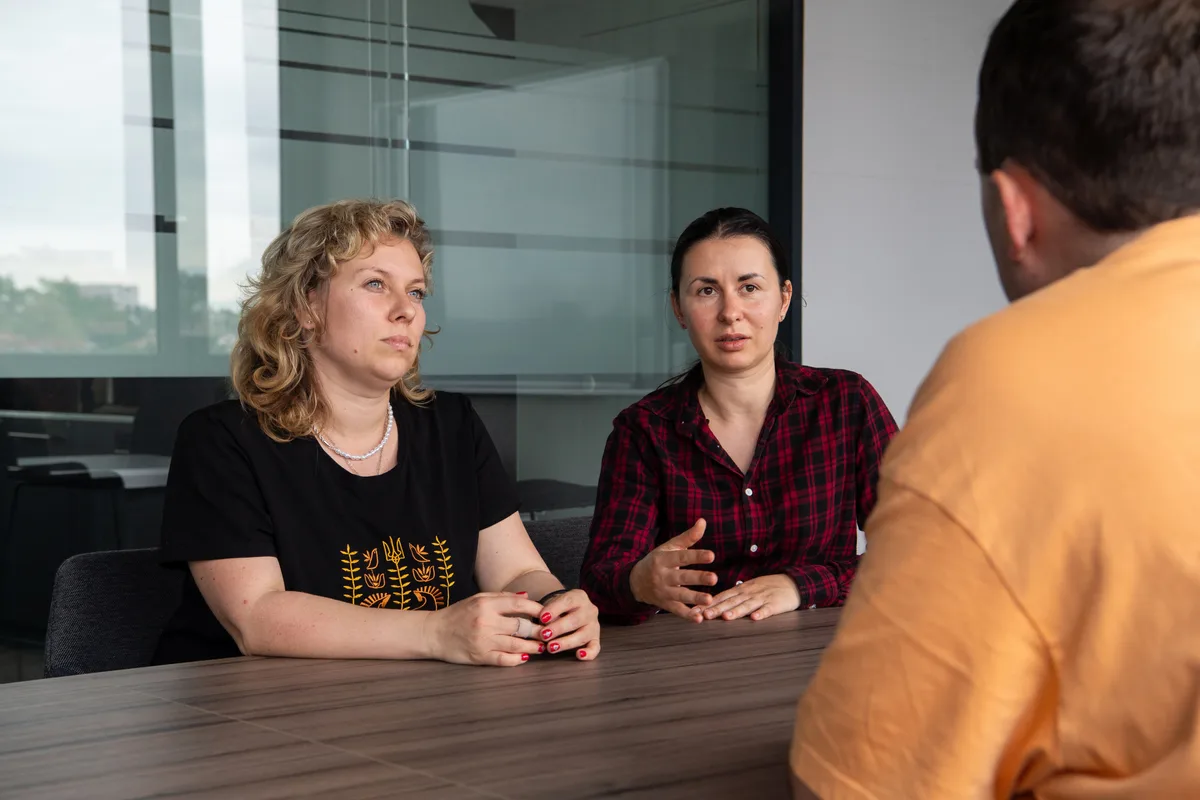 Olga Kostenko (links) und Halyna Yakovenko sprechen mit Marc K. über dessen nächsten Einsatz. Zwei Frauen sitzen einem Mann gegenüber. Den Mann sieht man nur von hinten.